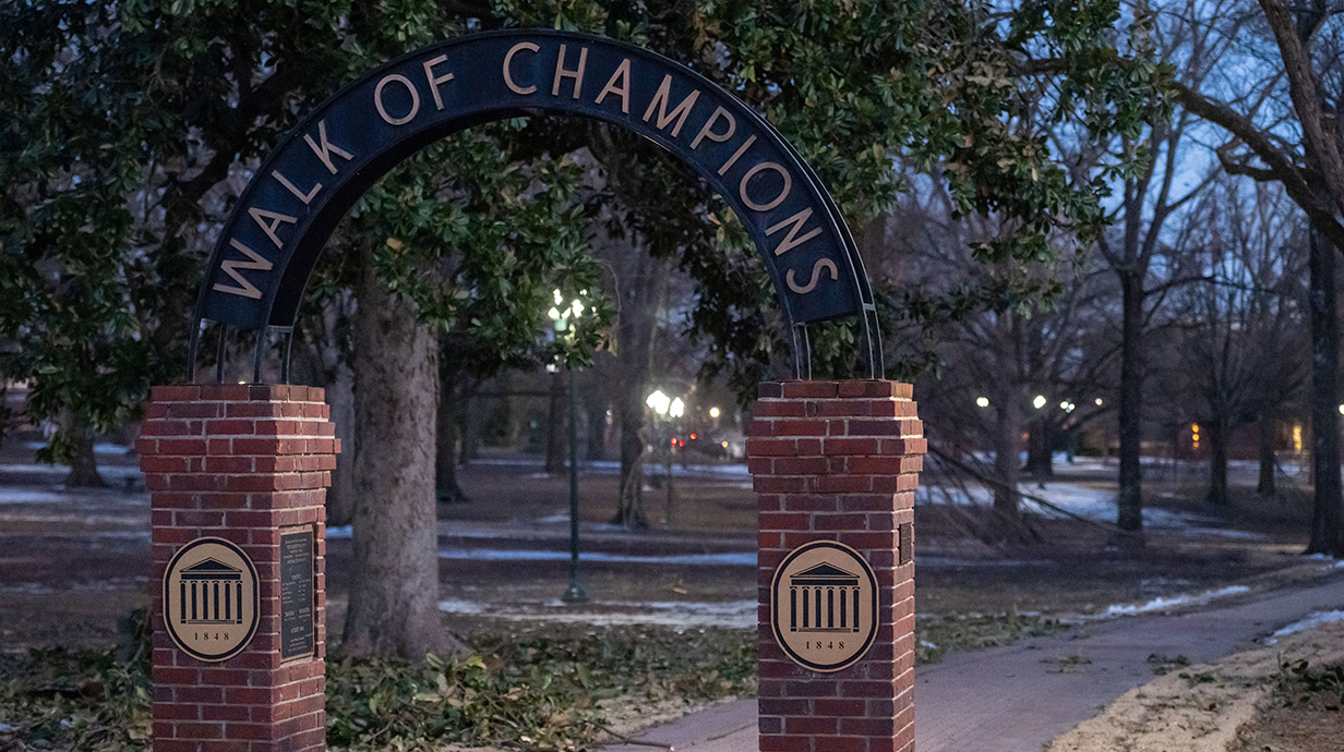 An archway reading Walk of Champions stands at the edge of a wooded park.
