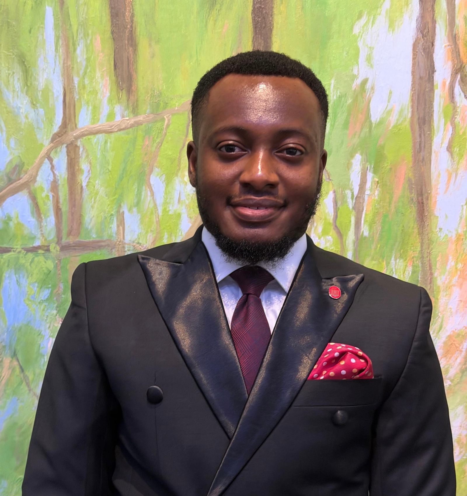 Godwin in a suit against a background of painted trees
