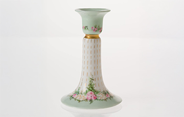 Hand-painted French porcelain candlestick with a pale green and white glaze, decorated with pink roses and gold accents along the shaft, flared base, and rim, photographed against a white background.