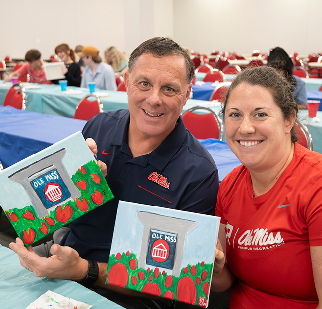 Two Ole Miss staff members show off their art at the Staff Appreciation Week 'Painting with Studio Whimzy' event
