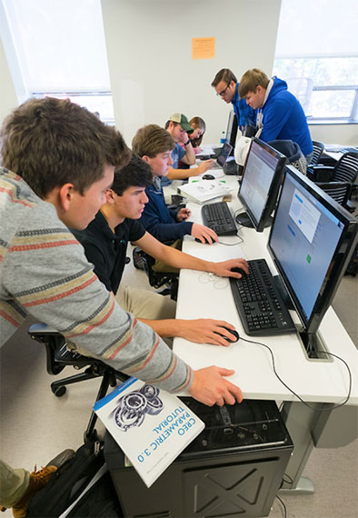 students in a computer lab with a CREO Parametric 3.0 Tutorial book in the foreground
