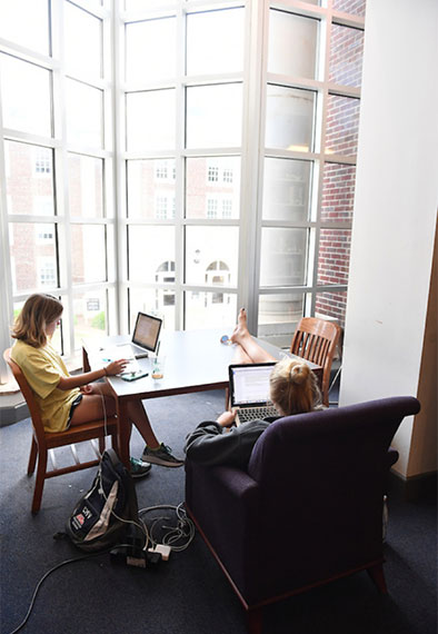 students lounging in the library while working on their laptops