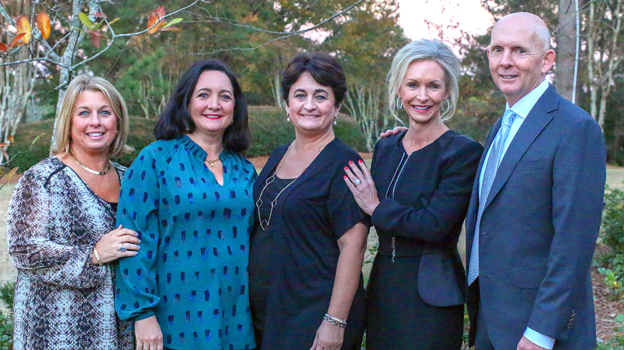 Four women and a man pose for an outdoor portrait.