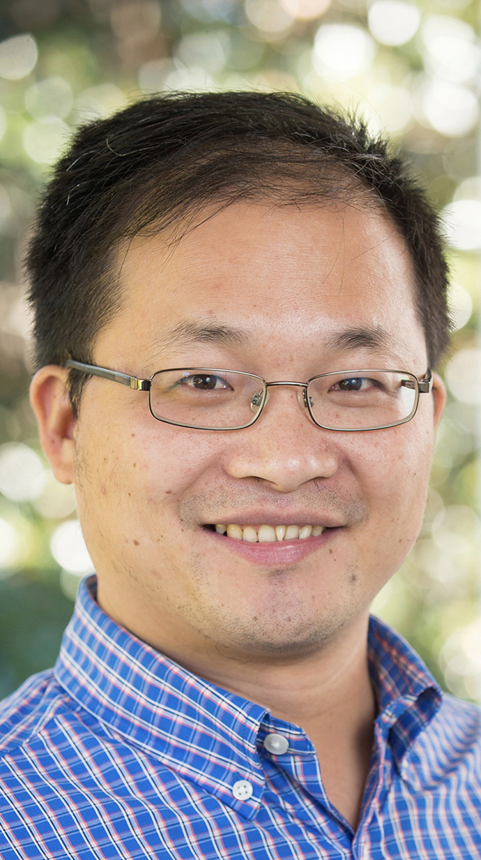 Headshot of a man wearing glasses and a blue checked shirt.