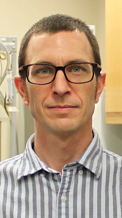 Headshot of a man wearing glasses and a gray striped shirt.