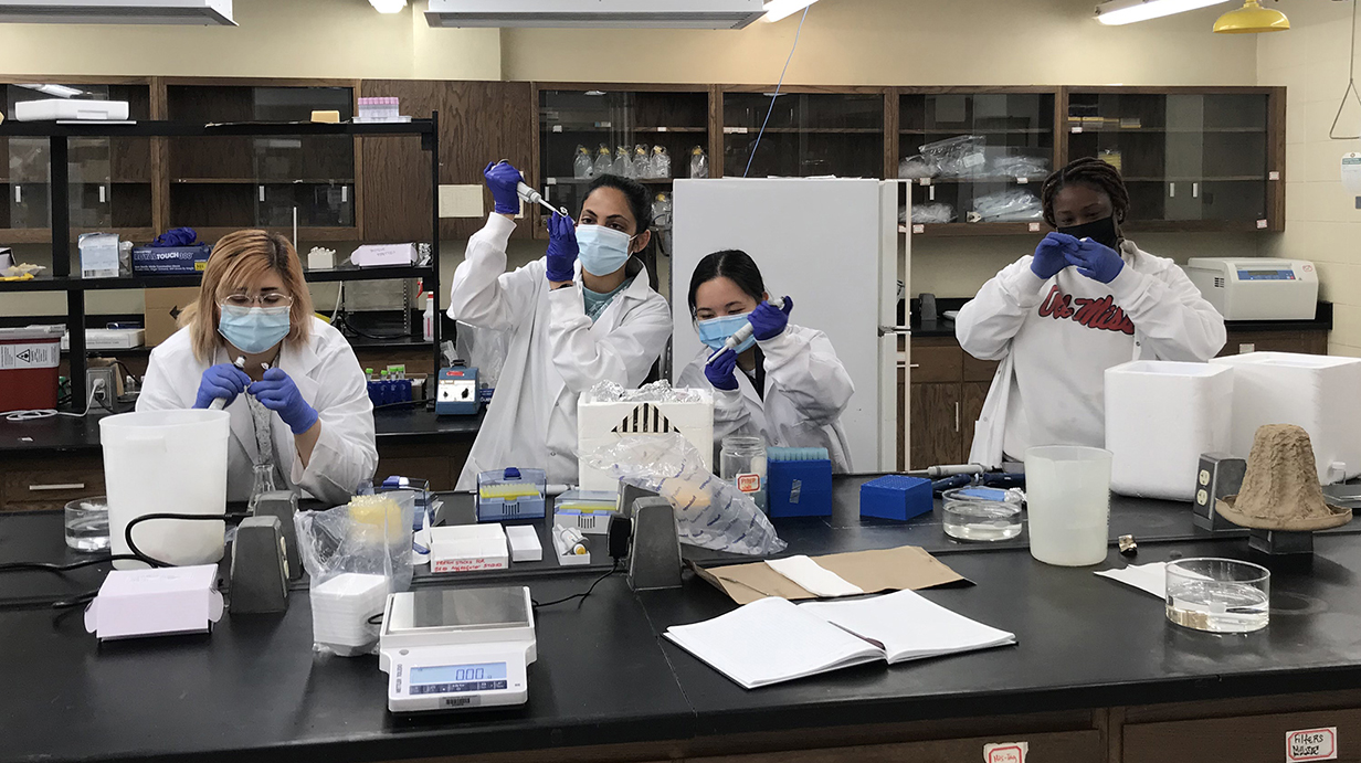 Four young women work with pipettes and test tubes in a laboratory.