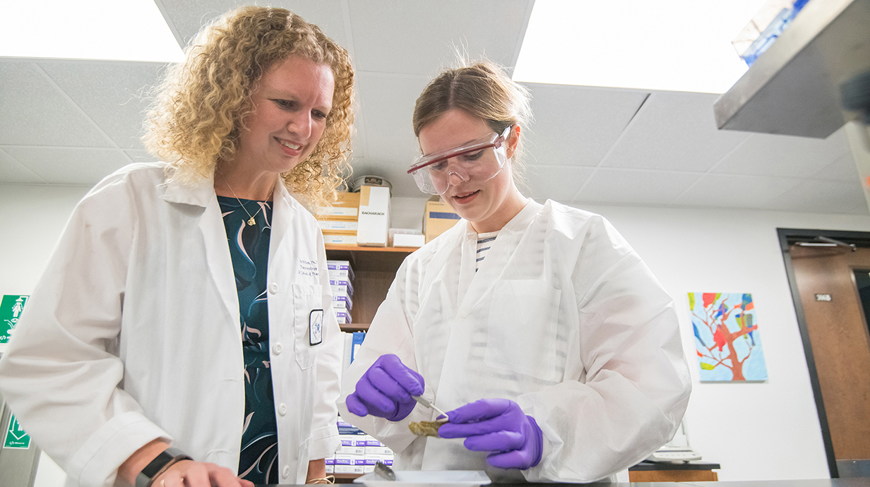 Two women wearing white lab coats examine a specimen in a laboratory.