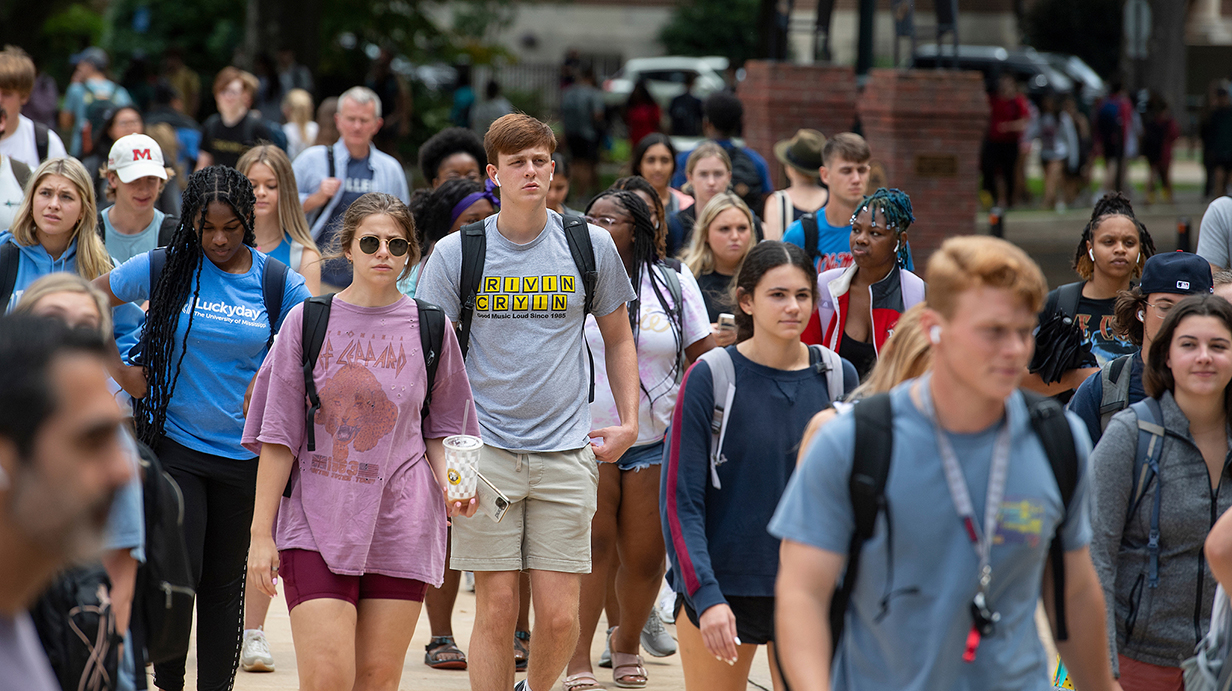 A large group of young people walk along a crowded sidewalk.