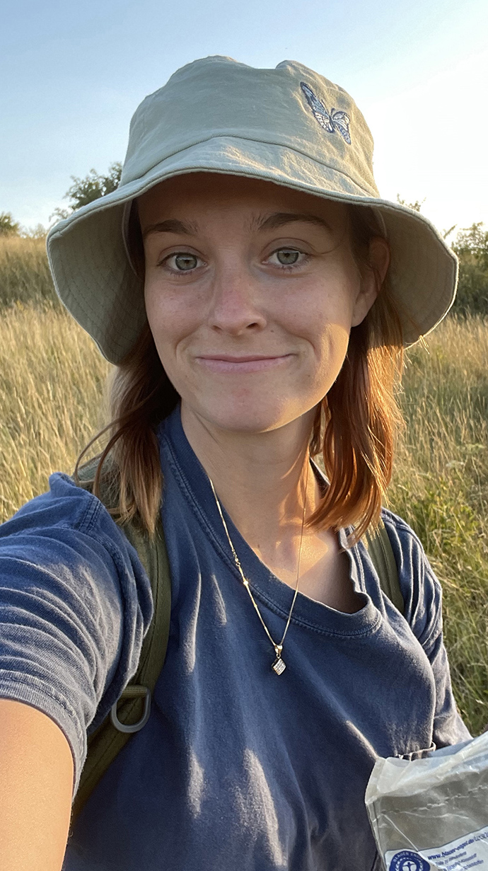 A young woman wearing a floppy hat takes a selfie outdoors.