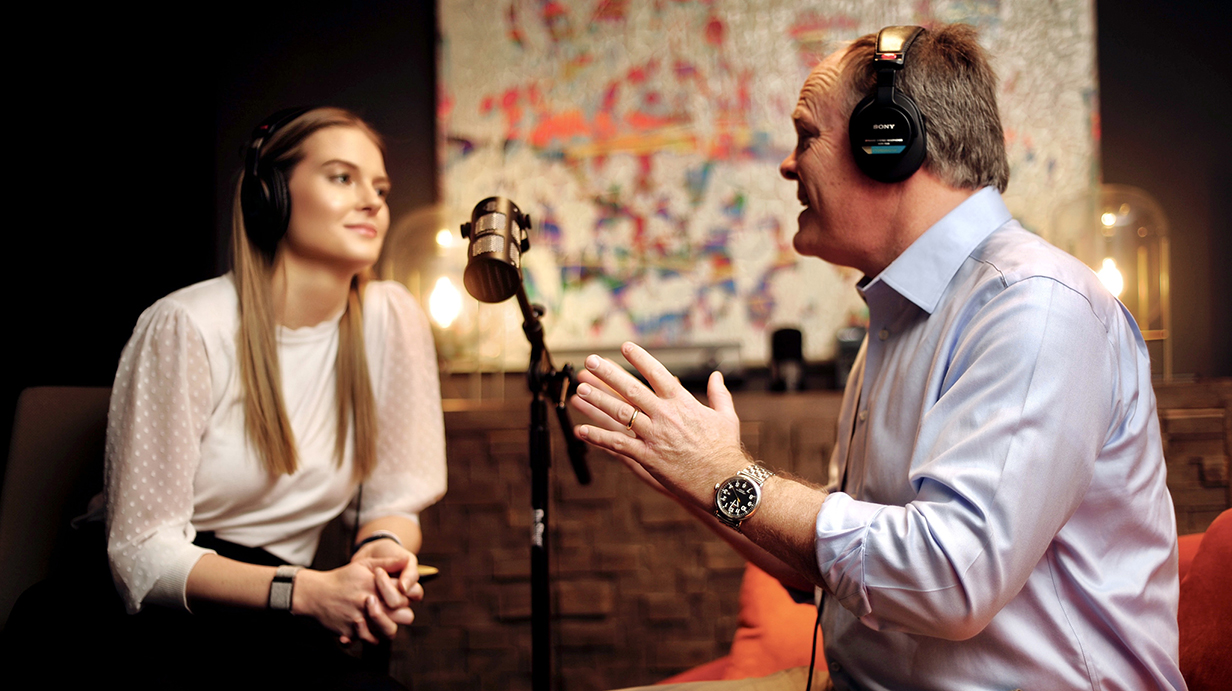 A man wearing headphones talks to a woman in a recording studio.