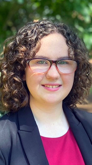 Headshot of a young woman wearing a dark blue jacket over a red blouse.