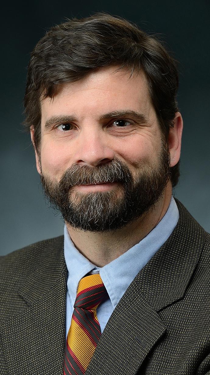 Headshot of a bearded man wearing a gray suit.
