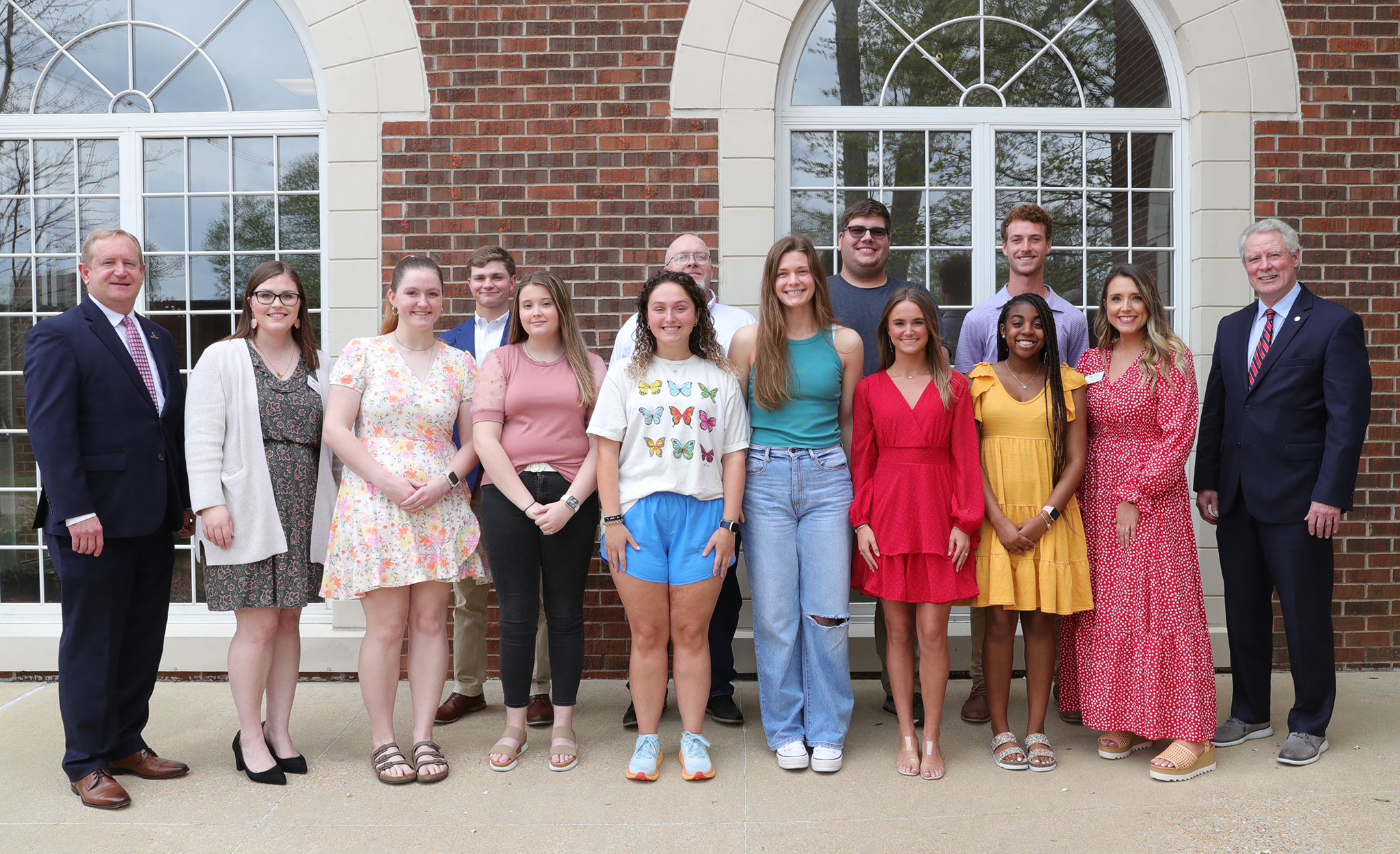 A group of students and university officials stand on the steps in front of a building. 