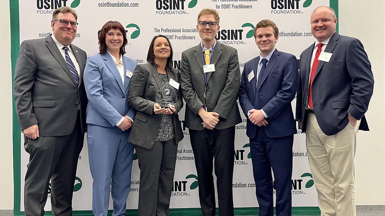A group of men and women, one holding a crystal trophy, stand in front of a printed backdrop for the OSINT Foundation.