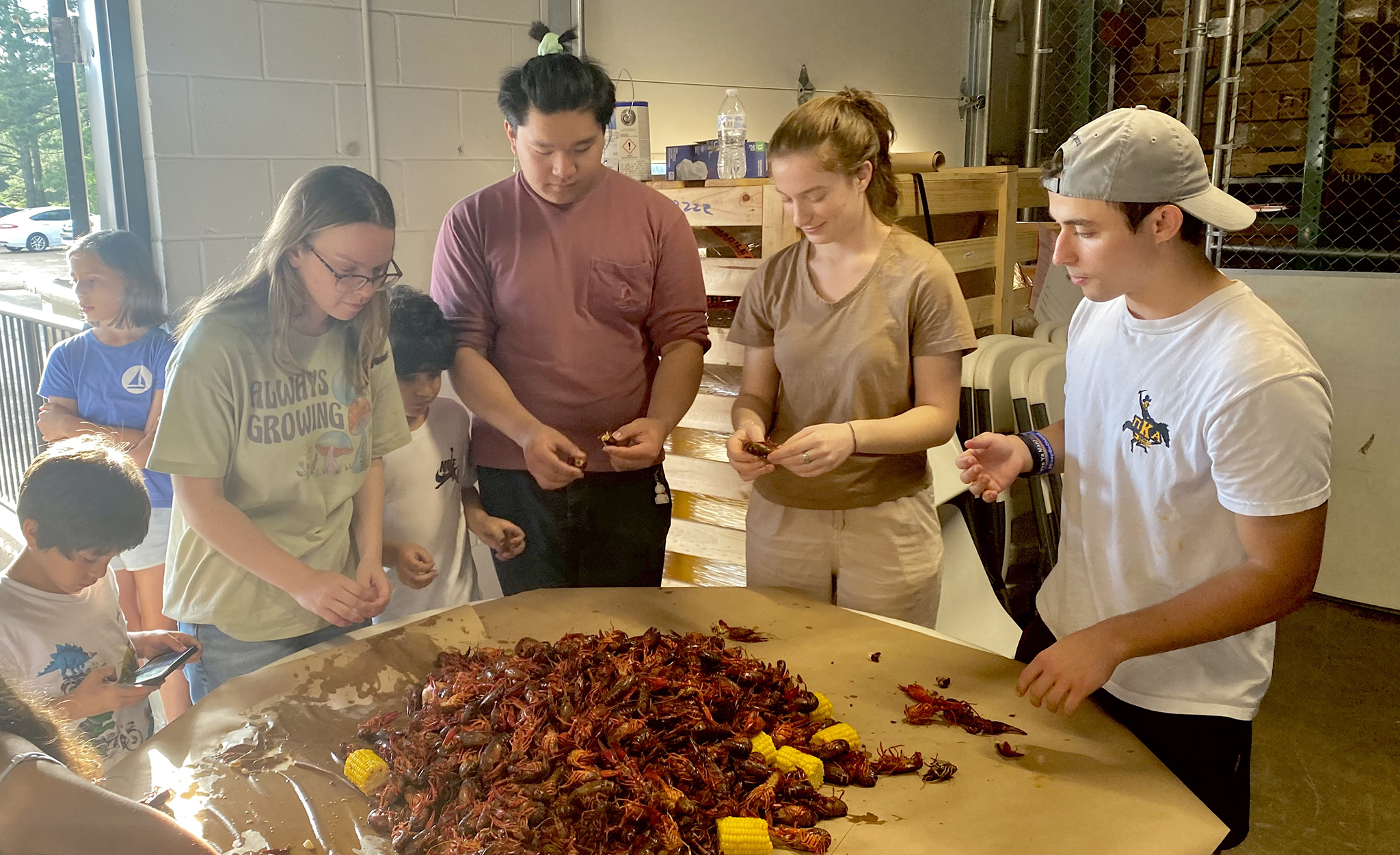 A group of people stand around a table peeling crawfish.