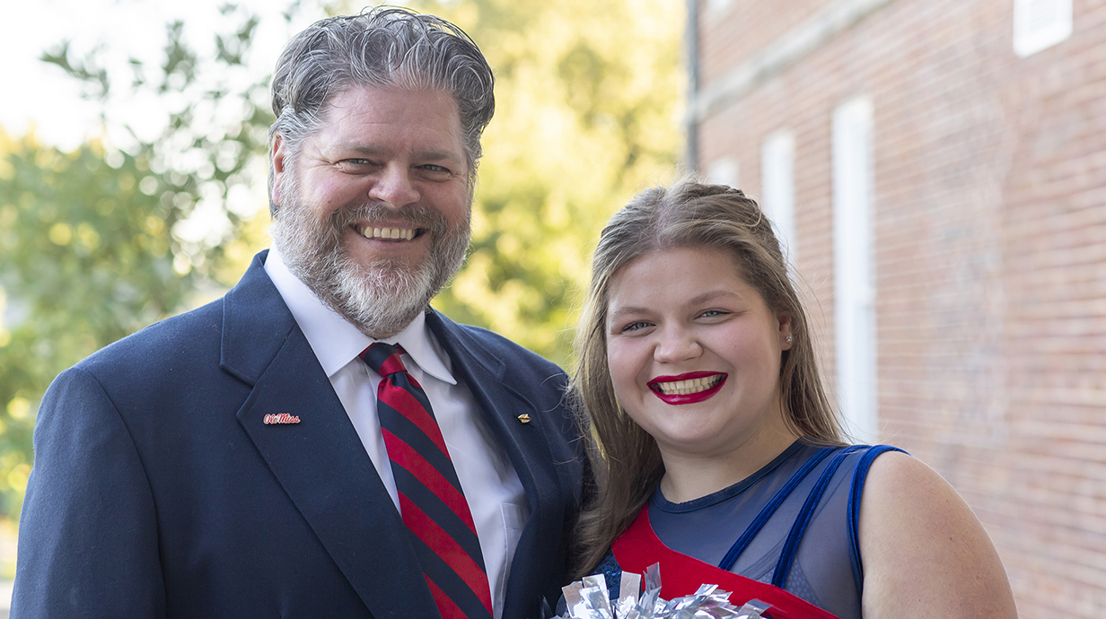 Photo of a man in a suit and a young woman wearing a band uniform.