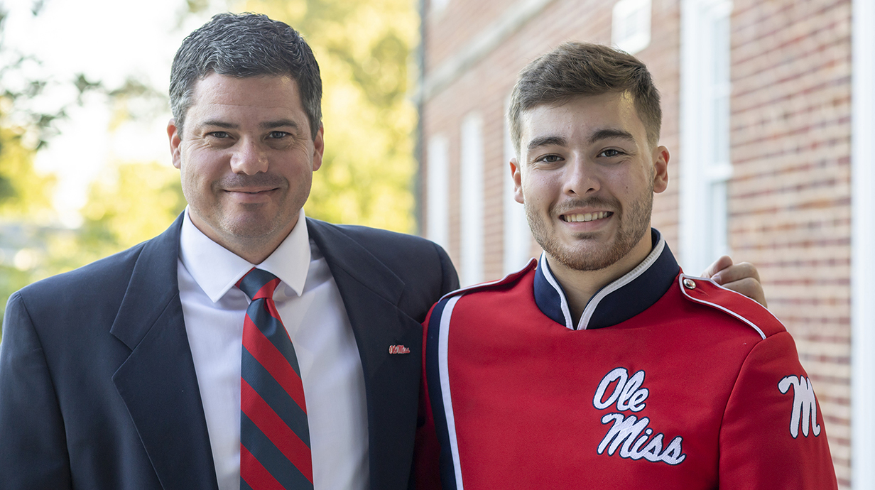 A man in a suit and a young man in a band uniform pose for a photo.