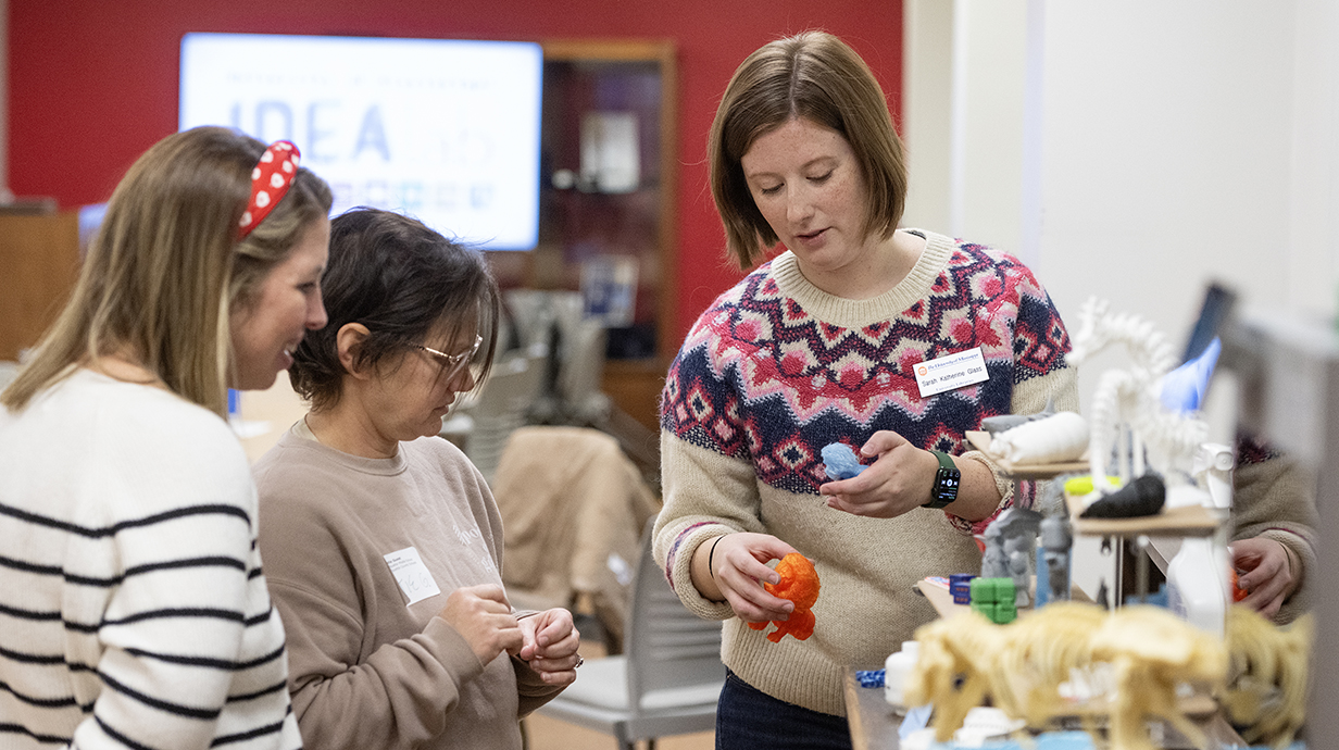 A woman shows a 3D-printed to two other women at a library conference.