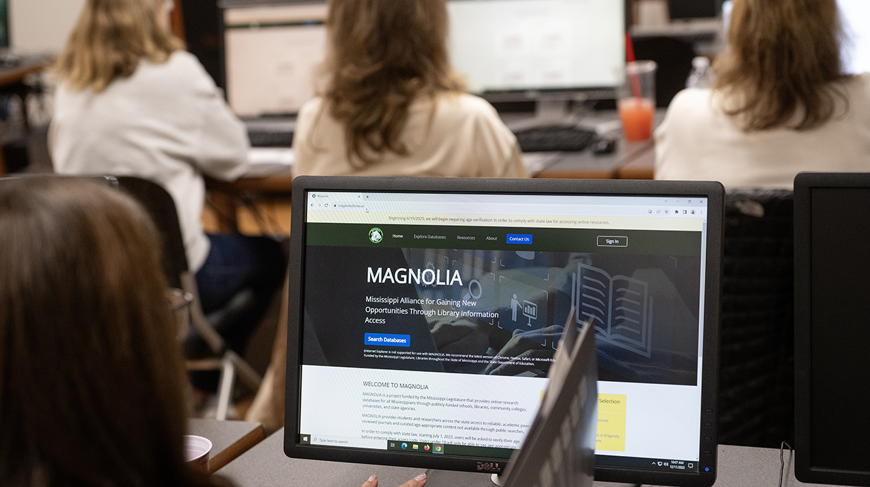 A woman looks at a computer screen displaying the MAGNOLIA logo.