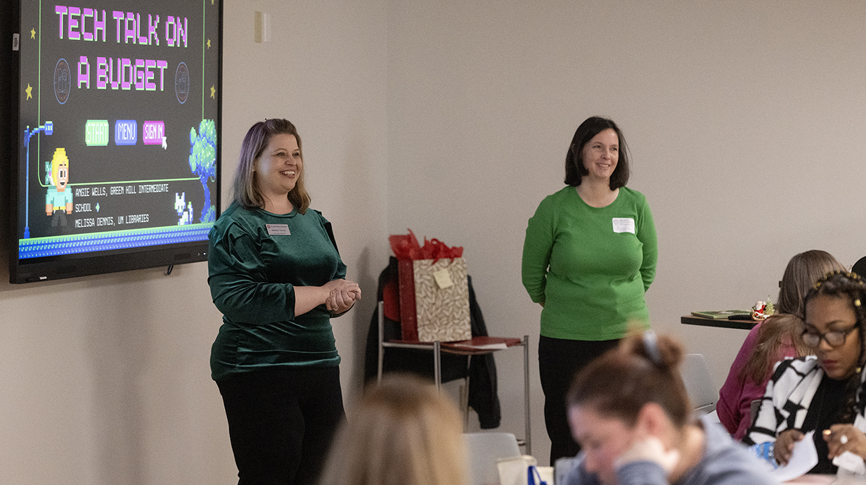 Two women speak to a group at a conference.