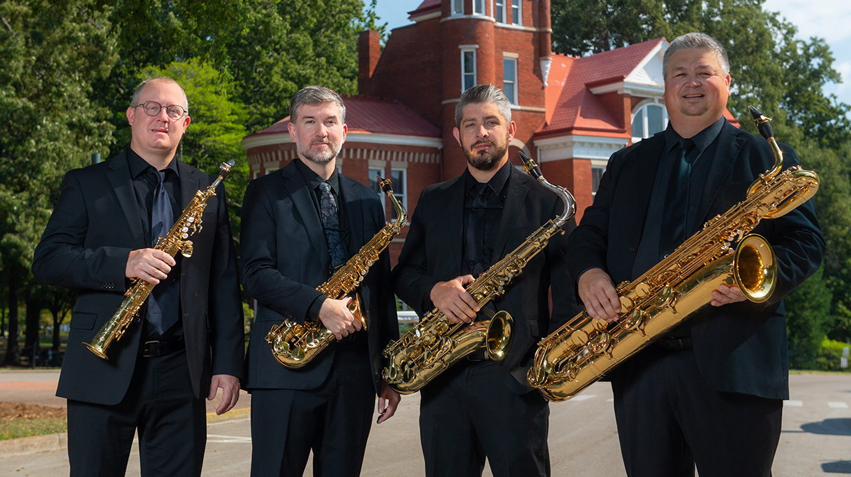 Four musicians stand outdoors holding saxophones