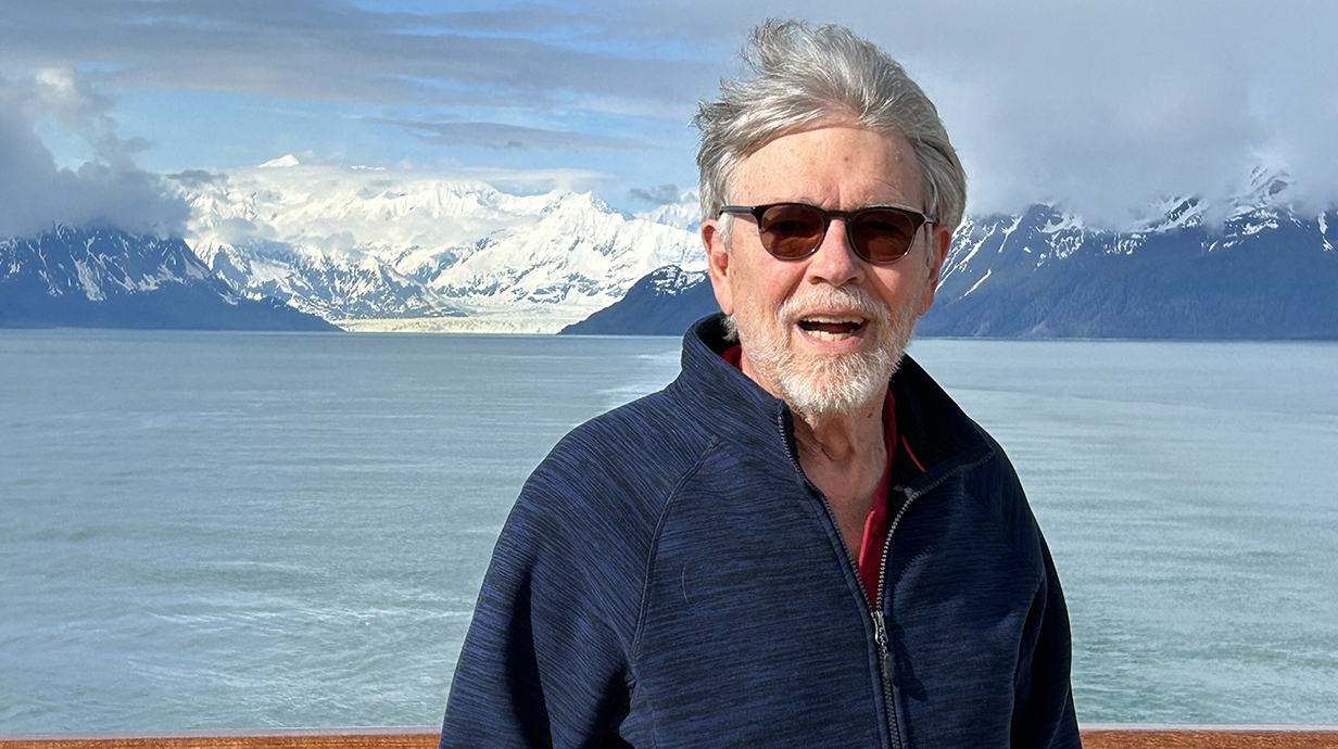 Michael Metcalf standing on the deck of a ship with snow-covered mountains in the background