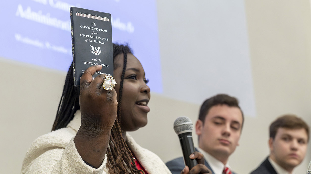 A woman holds up a printed copy of the U.S. Constitution while two young men watch.