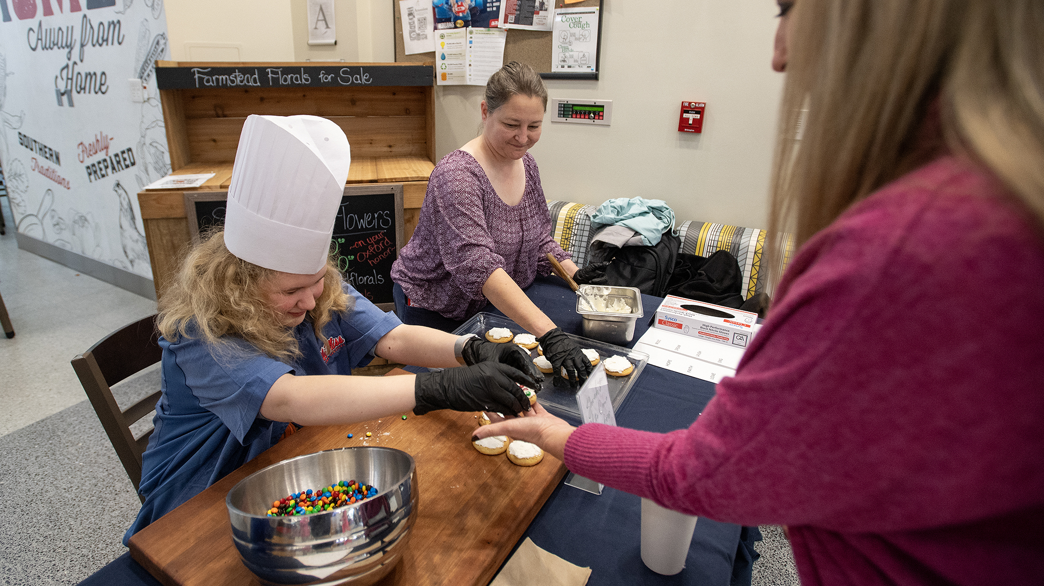 Student in chef hat hands a cookie to a visitor at Rebel Market.