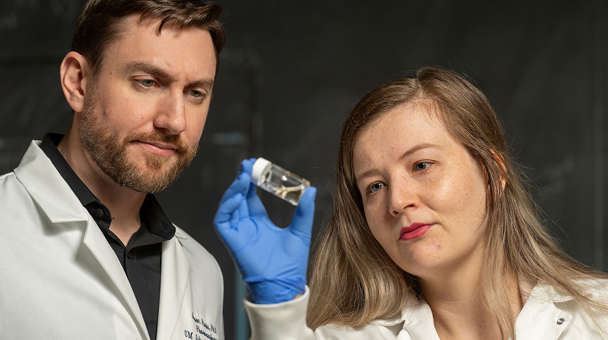 A man and a woman examine a vial of liquid in a lab.