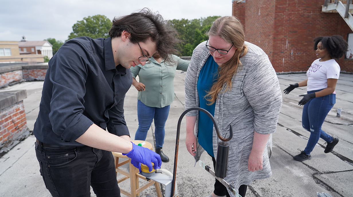 Man and woman examine scientific instruments on a rooftop.