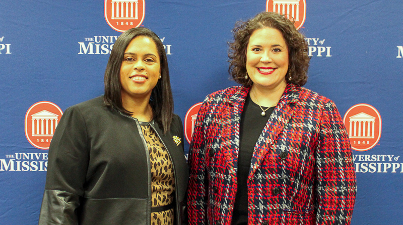 Two women stand in front of an Ole Miss background.