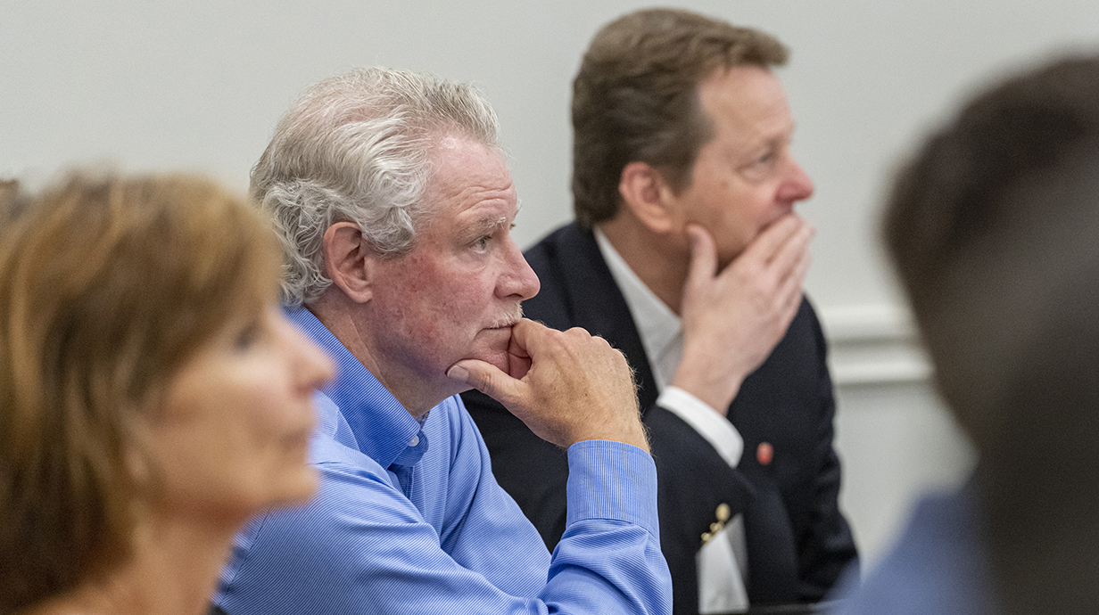 Two men and a woman look at a speaker out of the frame.