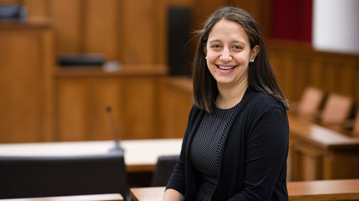 A woman sits smiling in an empty courtroom.