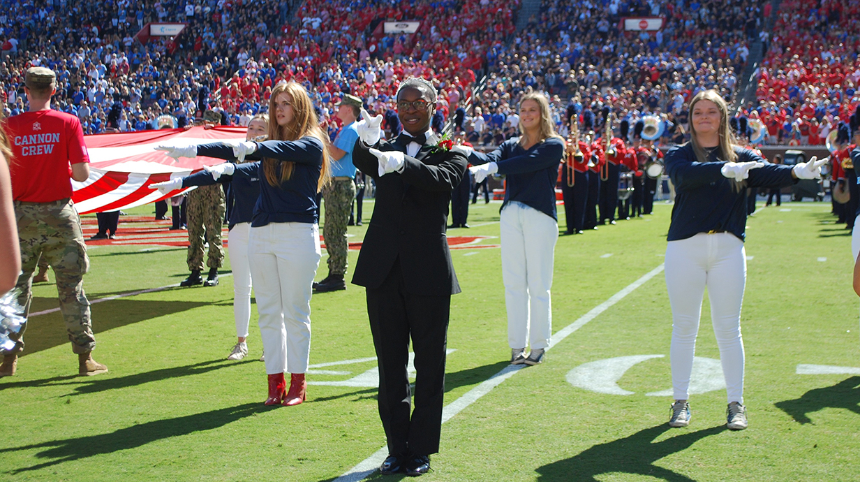 A young man and three young women perform American Sign Language on a football field.