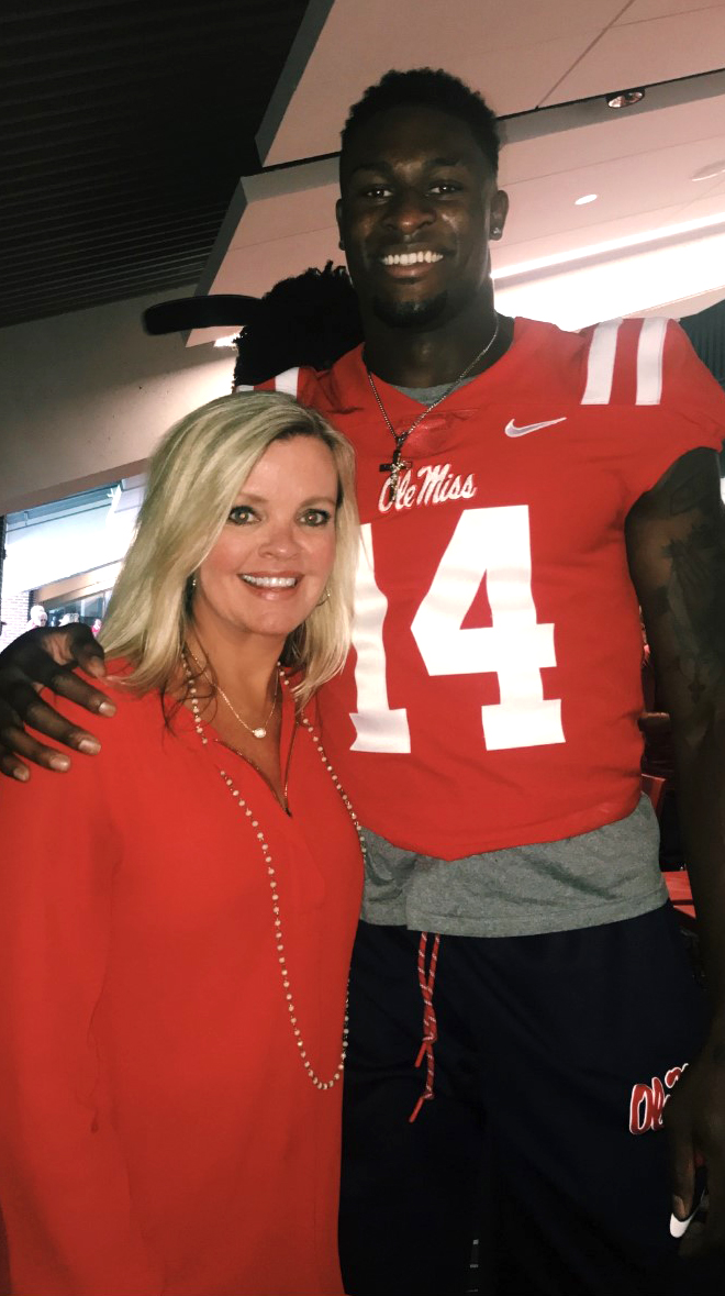 A woman in a red dress stands next to a football player in uniform.