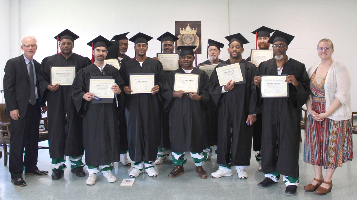 A man and a woman stand with a group of men in black robes holding certificates.