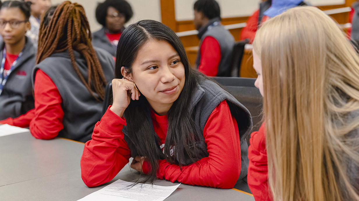 Two female high school students talk in a classroom.