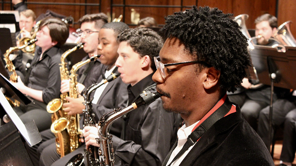 A row of band students play saxophones during a concert onstage.