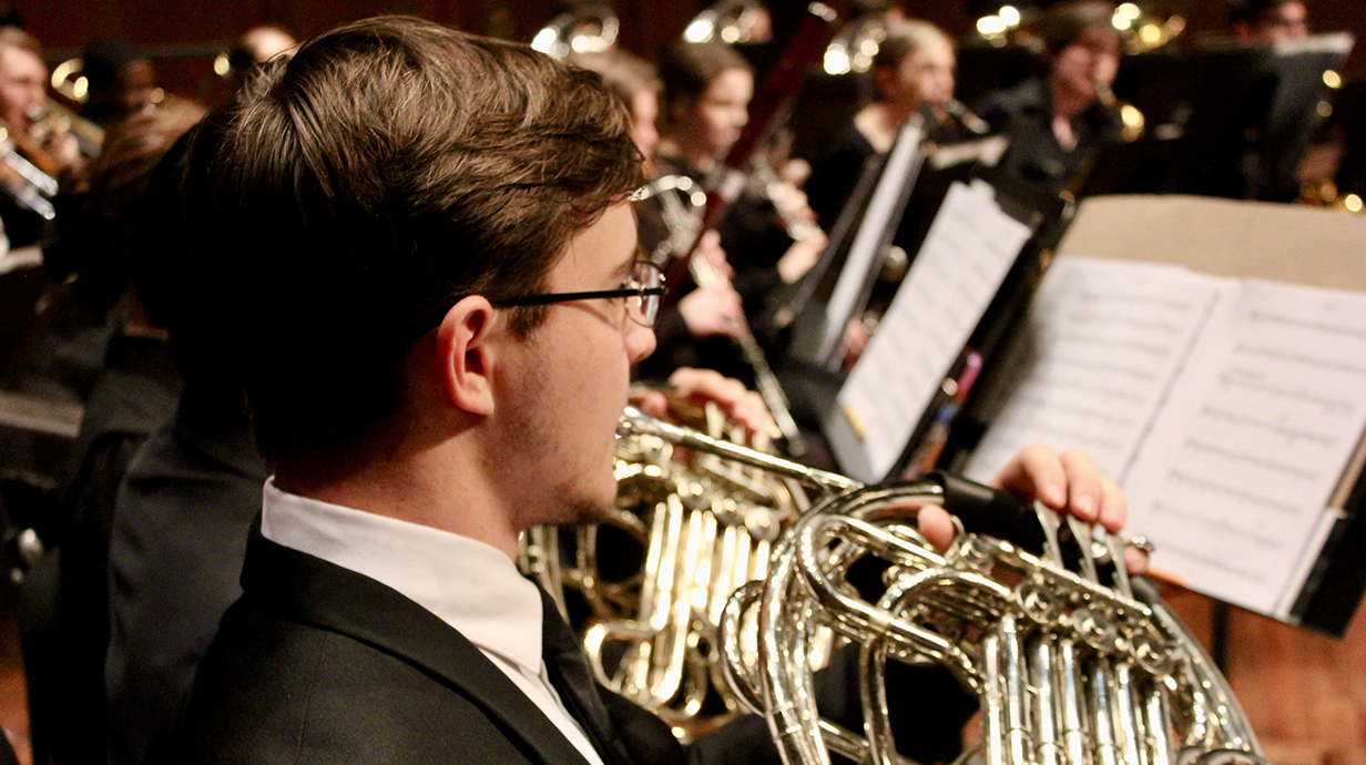 A musician plays French horn as part of an orchestra.