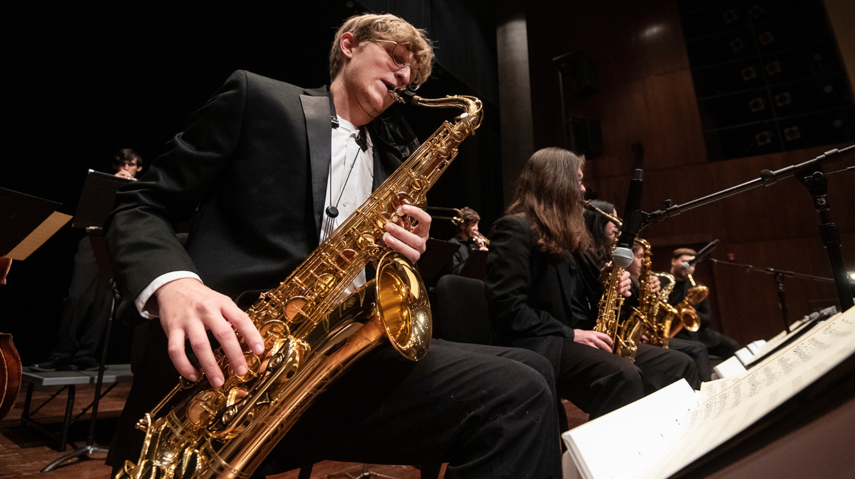 A row of musicians play saxophones opnstage.