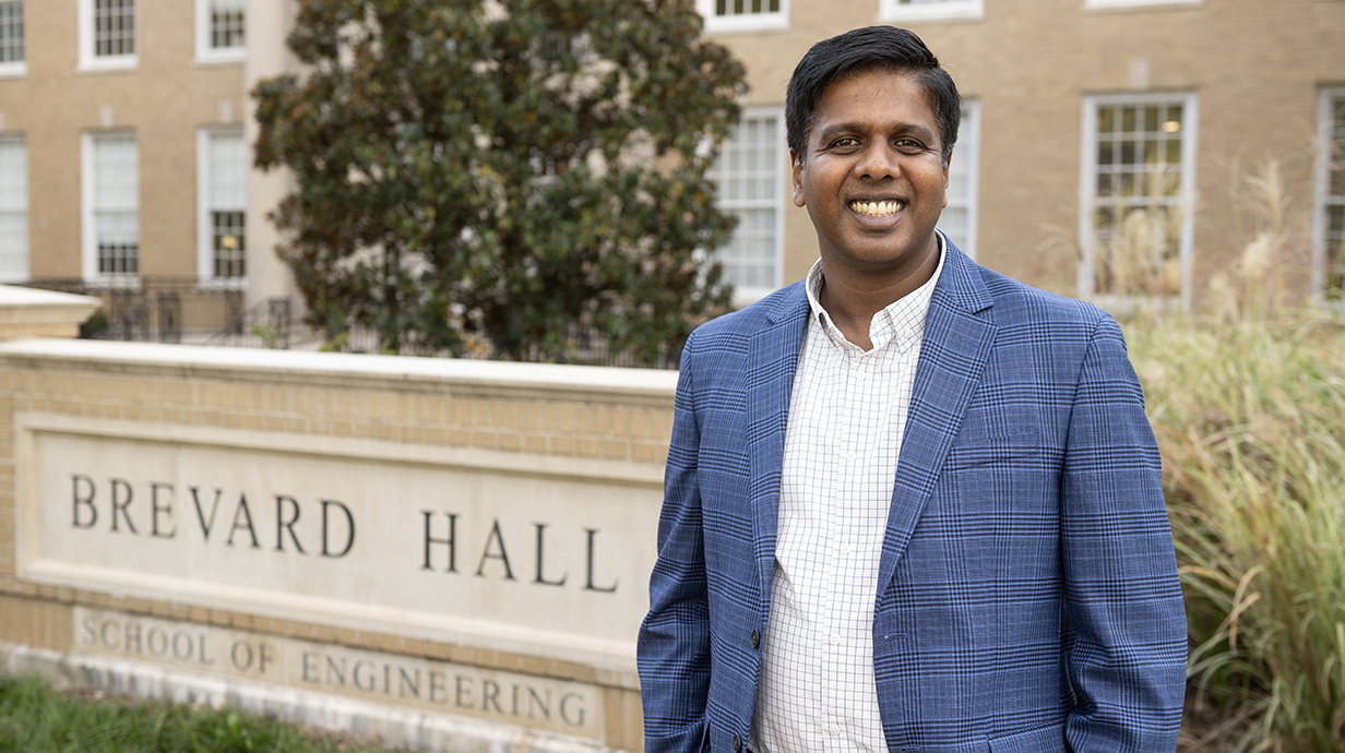 A man stands outdoors in front of a sign reading 'Brevard Hall: School of Engineering.'