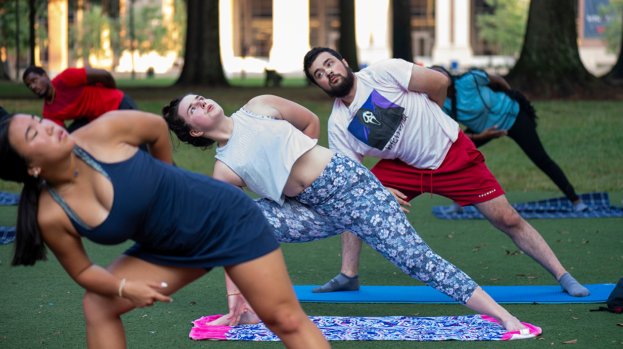 A group of young women and men practice yoga poses outdoors.