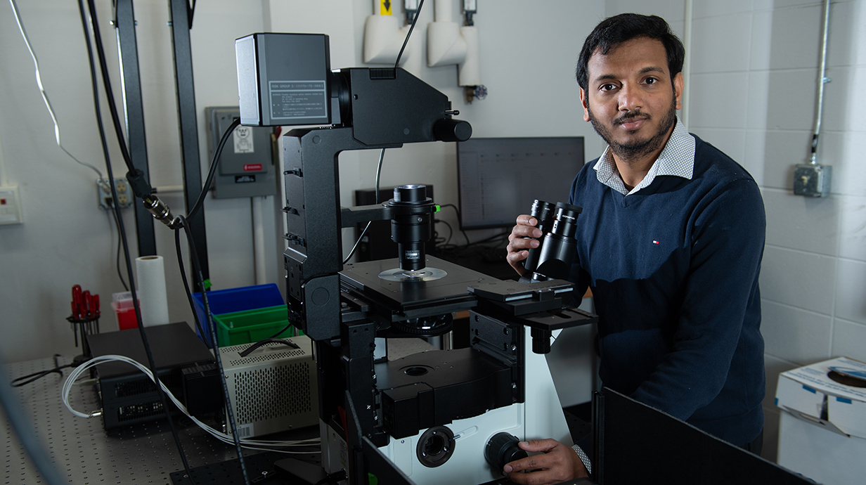 A man stands behind a microscope in a laboratory.