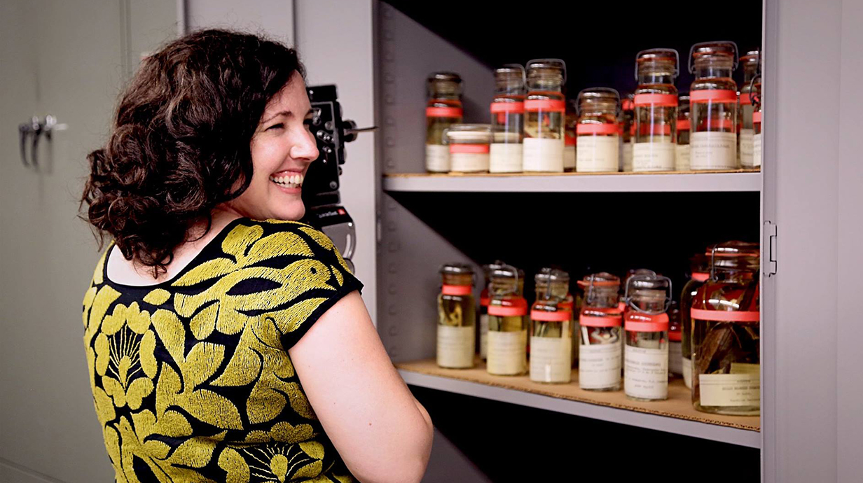 A woman reaches into a cabinet lined with glass jard.