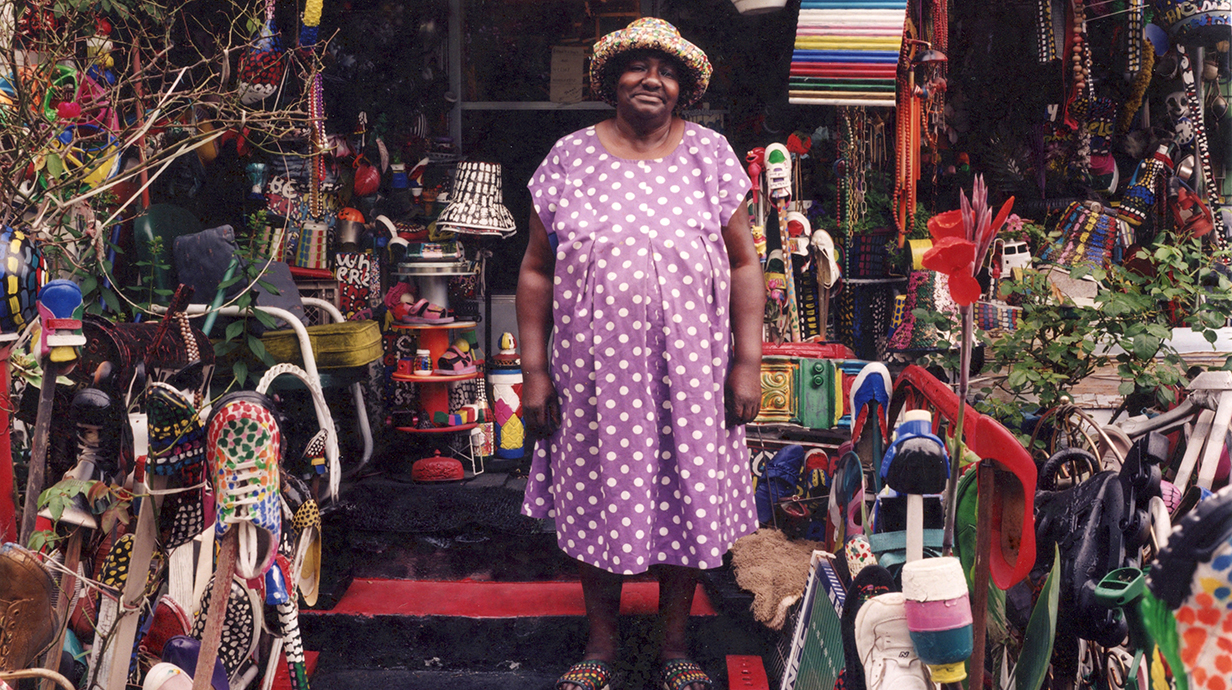 A woman stands on the front porch of a house, surrounded by artworks.