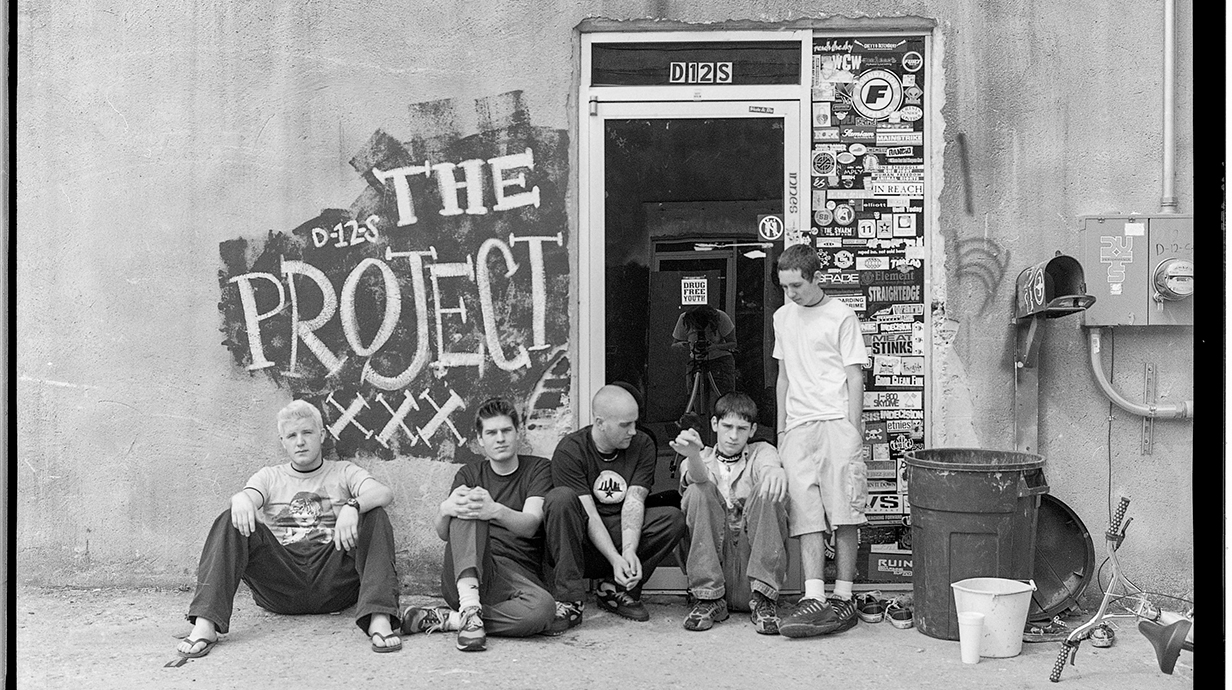 A group of young people sit outside an open warehouse door.