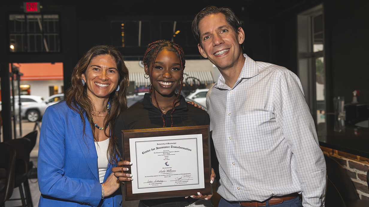 A woman and a man congratulate a young woman holding an award certificate.