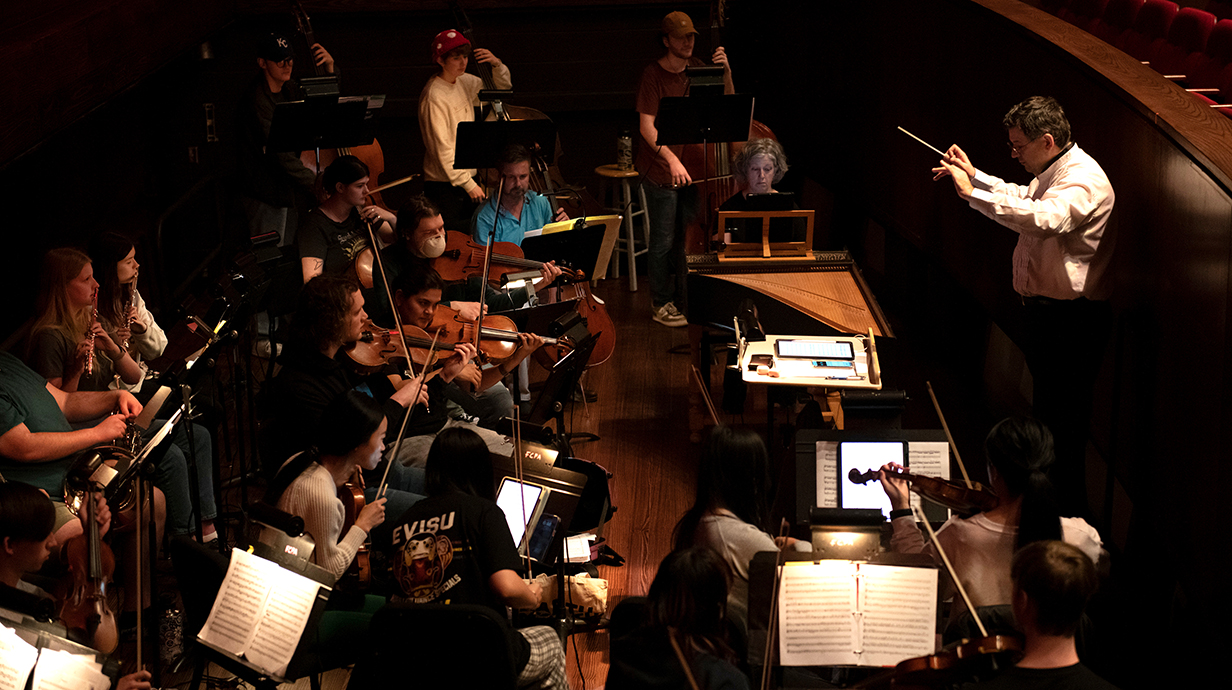 A conductor leads an orchestra through a warm-up before a performance.