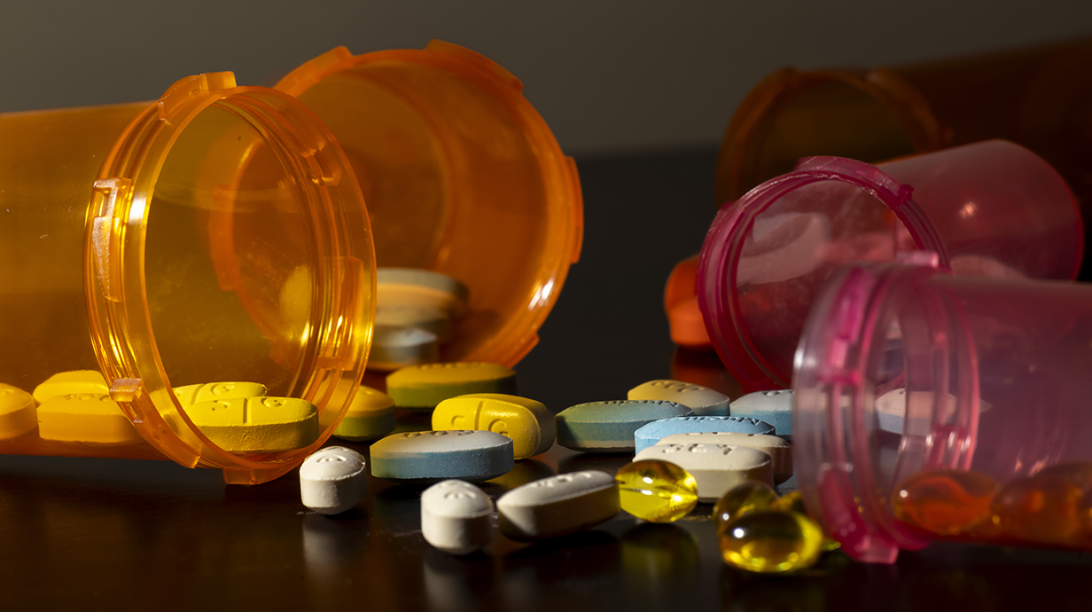Several pill bottles lie open surrounding a small pile of pills.