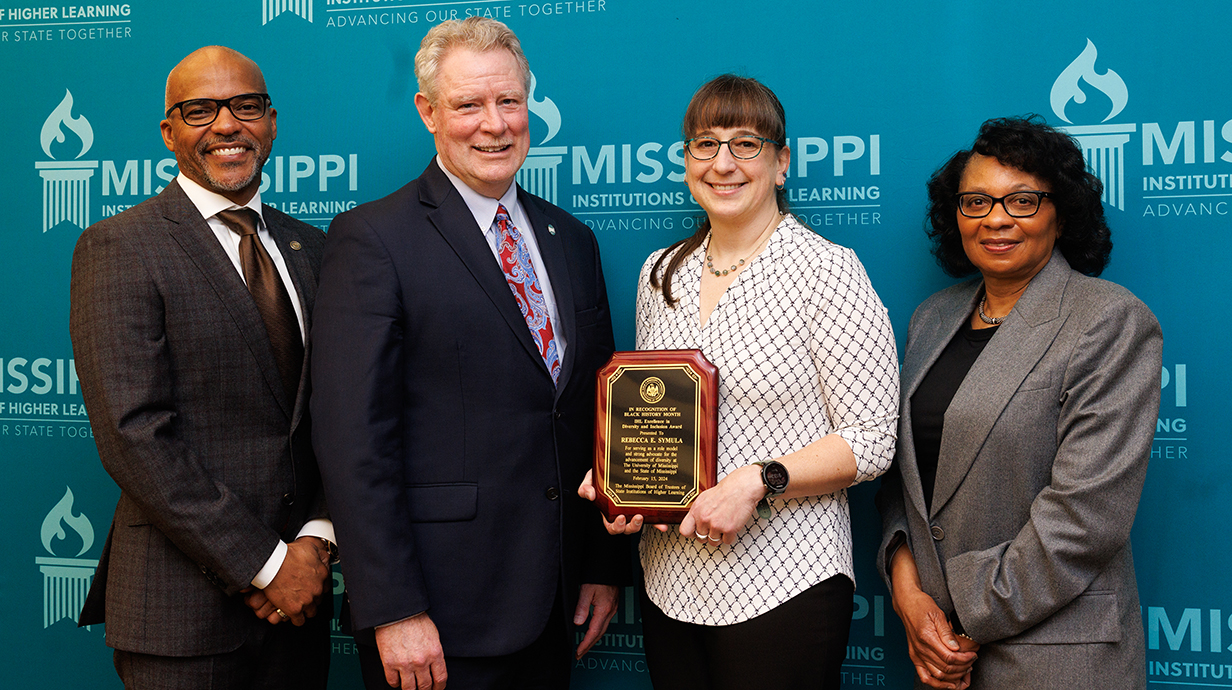 Four people in a group with Rebecca Symula holding an award plaque